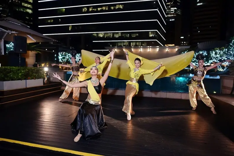 Cultural dance troupe in kebaya and gold costumes performing with yellow silk scarves on a poolside deck at night in Singapore